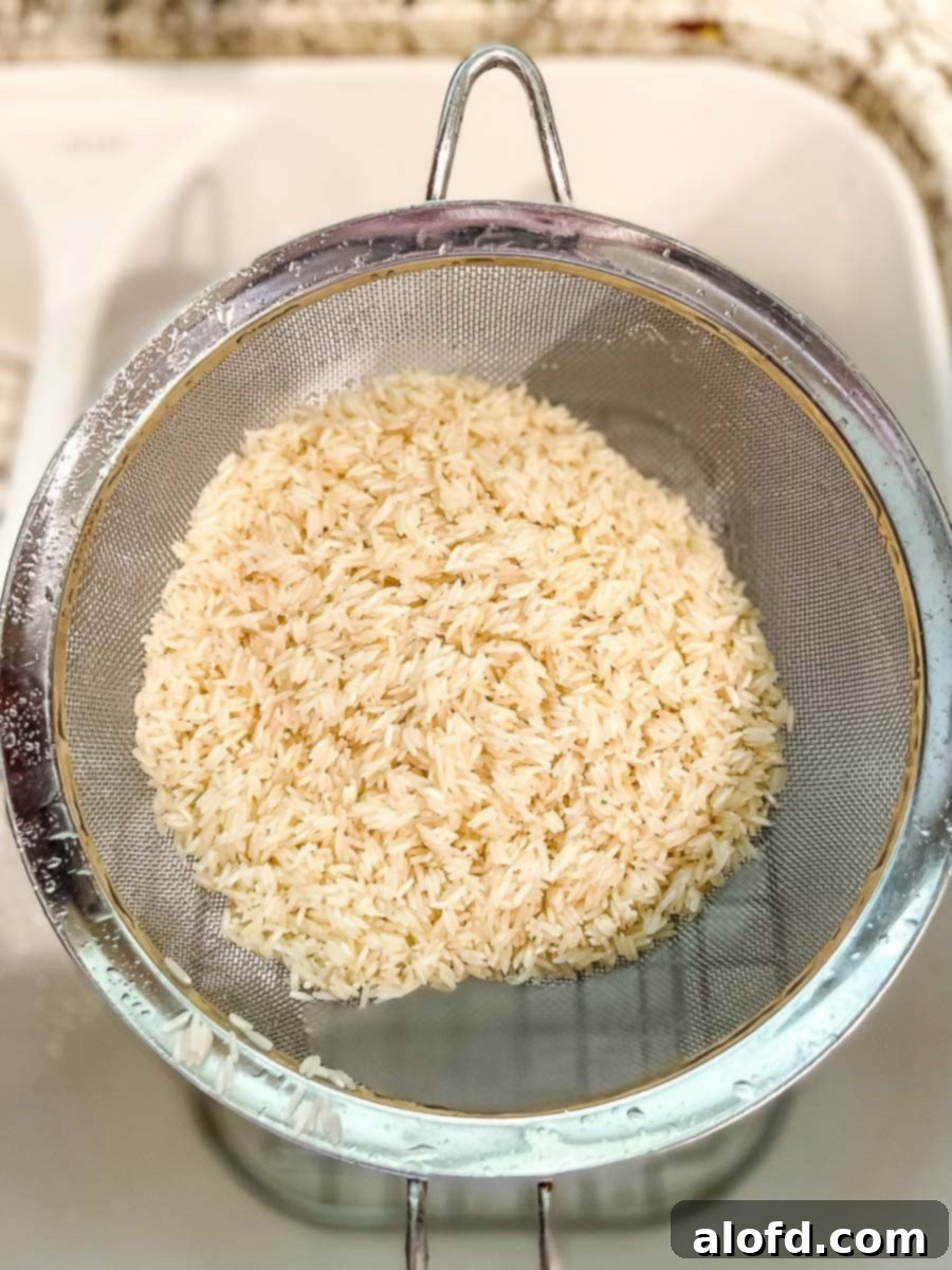 Close-up of jasmine rice being rinsed in a mesh colander under cold water, highlighting the importance of washing away excess starch.