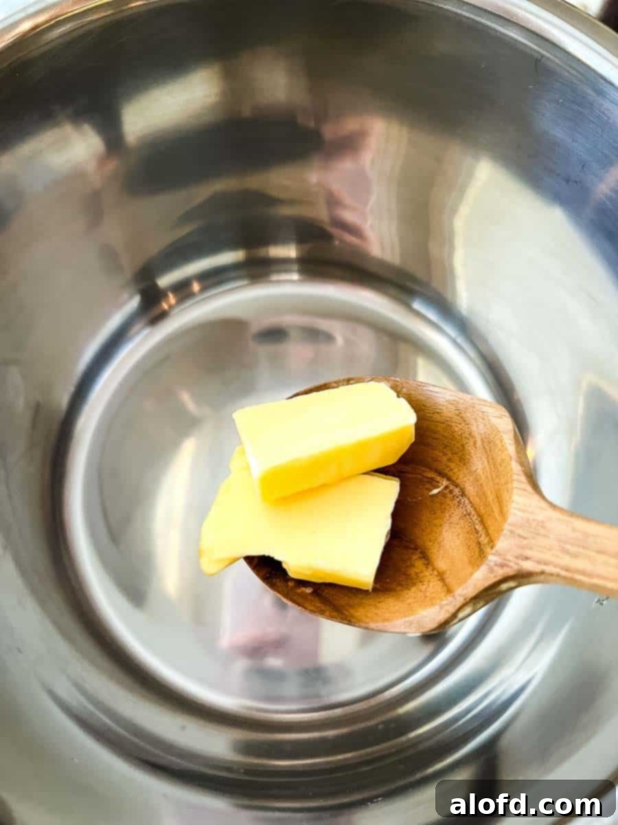A wooden spoon carefully placing a pat of butter into the hot Instant Pot, preparing for the sautéing stage of the jasmine rice recipe.