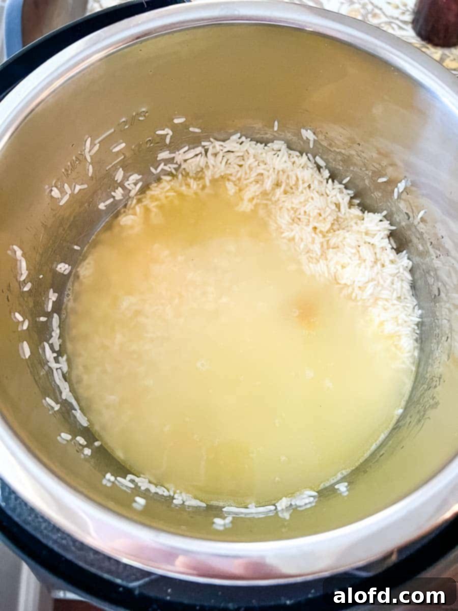Chicken broth has just been added to the sautéed Jasmine rice in the Instant Pot, ready for pressure cooking. The liquid perfectly covers the grains.
