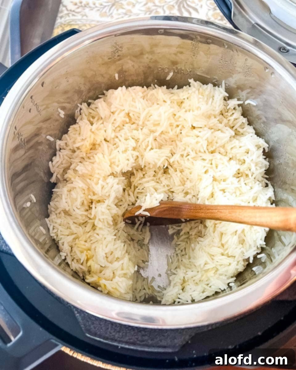 A close-up shot of fluffy Instant Pot Jasmine Rice being gently fluffed with a fork in the inner pot, ready for serving.