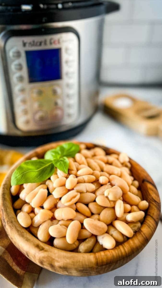 Perfectly Tender Instant Pot Cannellini Beans 3 A close-up shot of a wooden bowl filled with creamy white cannellini beans, adorned with a fresh basil sprig. The background shows an Instant Pot and a patterned napkin.