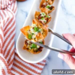 A hand and tong holding a jalapeno popper wonton cup and a serving tray full of jalapeno wonton popper cups and a striped red cloth in the background.