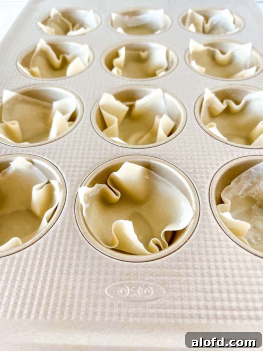 Wonton wrappers all lined up in a muffin pan, shaped into cups.
