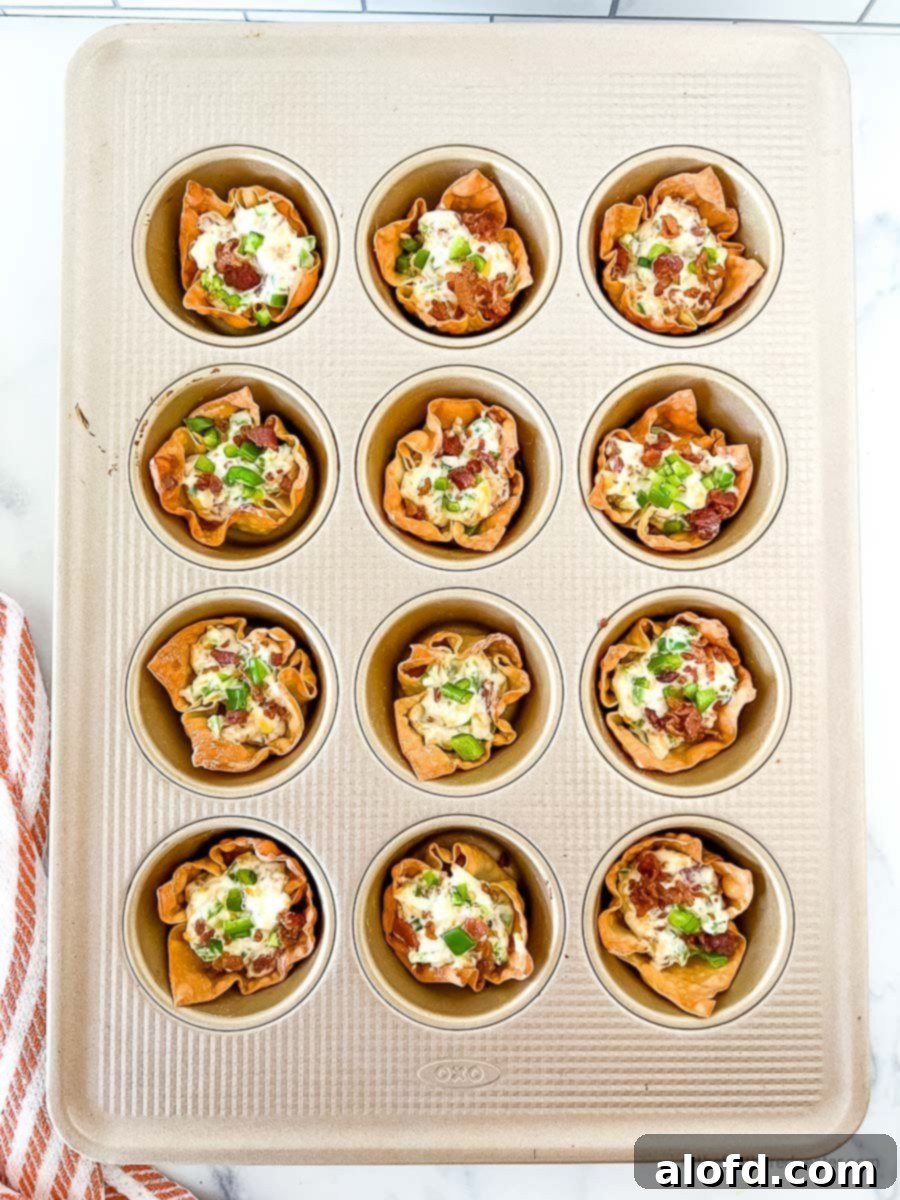 Jalapeno popper filling mixture inside the wonton cups on a muffin pan, ready for final baking.