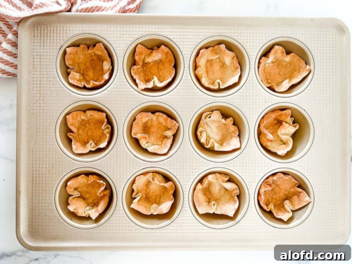 Crispy Baked Wonton Delights 8 A muffin tin with perfectly baked wonton wrapper cups, accompanied by a red striped kitchen towel on the side.