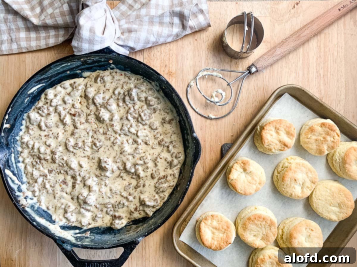 A glistening cast iron skillet filled with homemade sausage gravy, next to a golden pan of freshly baked biscuits, ready to be served and enjoyed for a comforting meal.