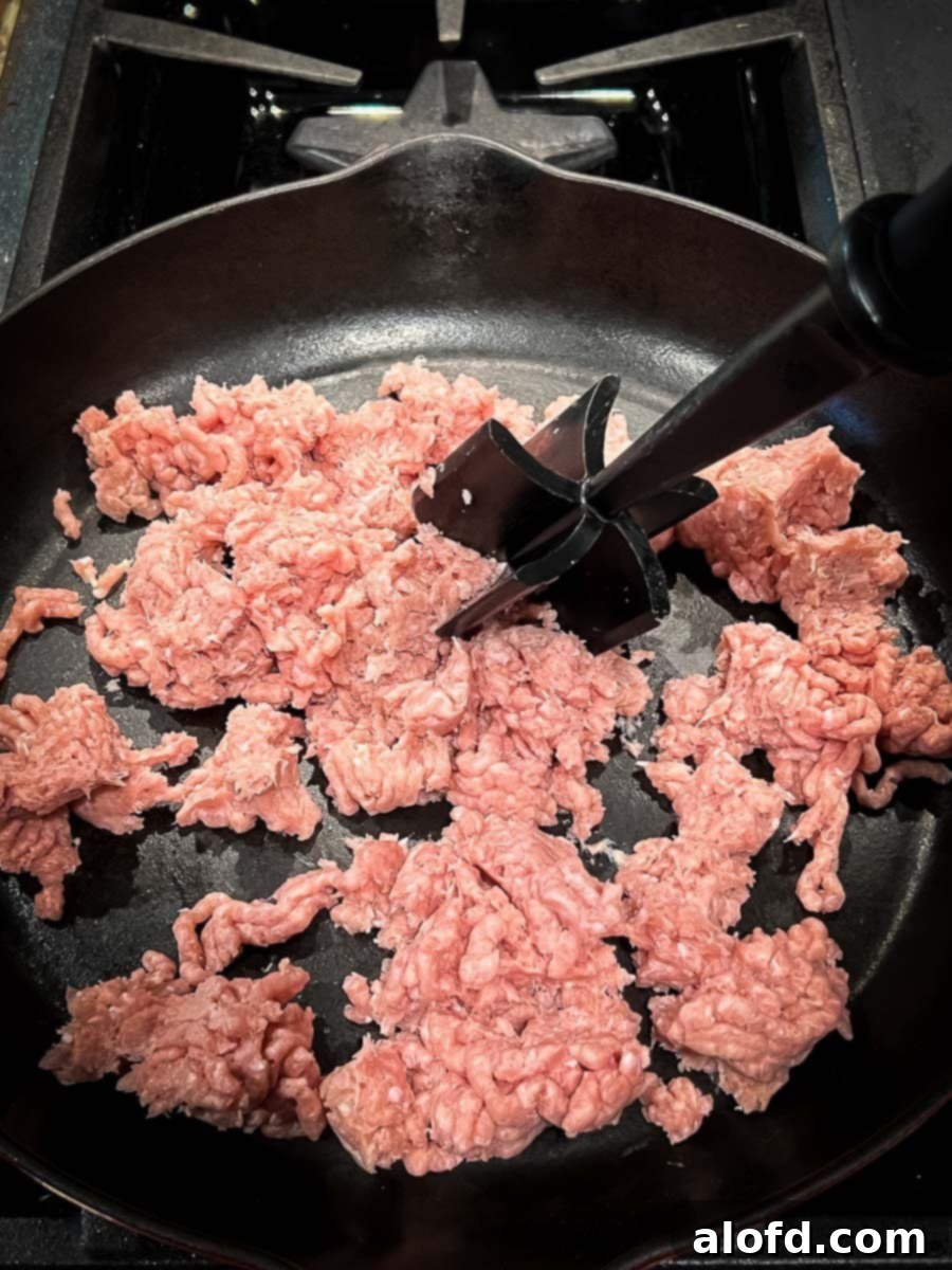Close-up of ground turkey browning in a black cast iron skillet over medium heat, with steam gently rising, showcasing the beginning of the gravy-making process.