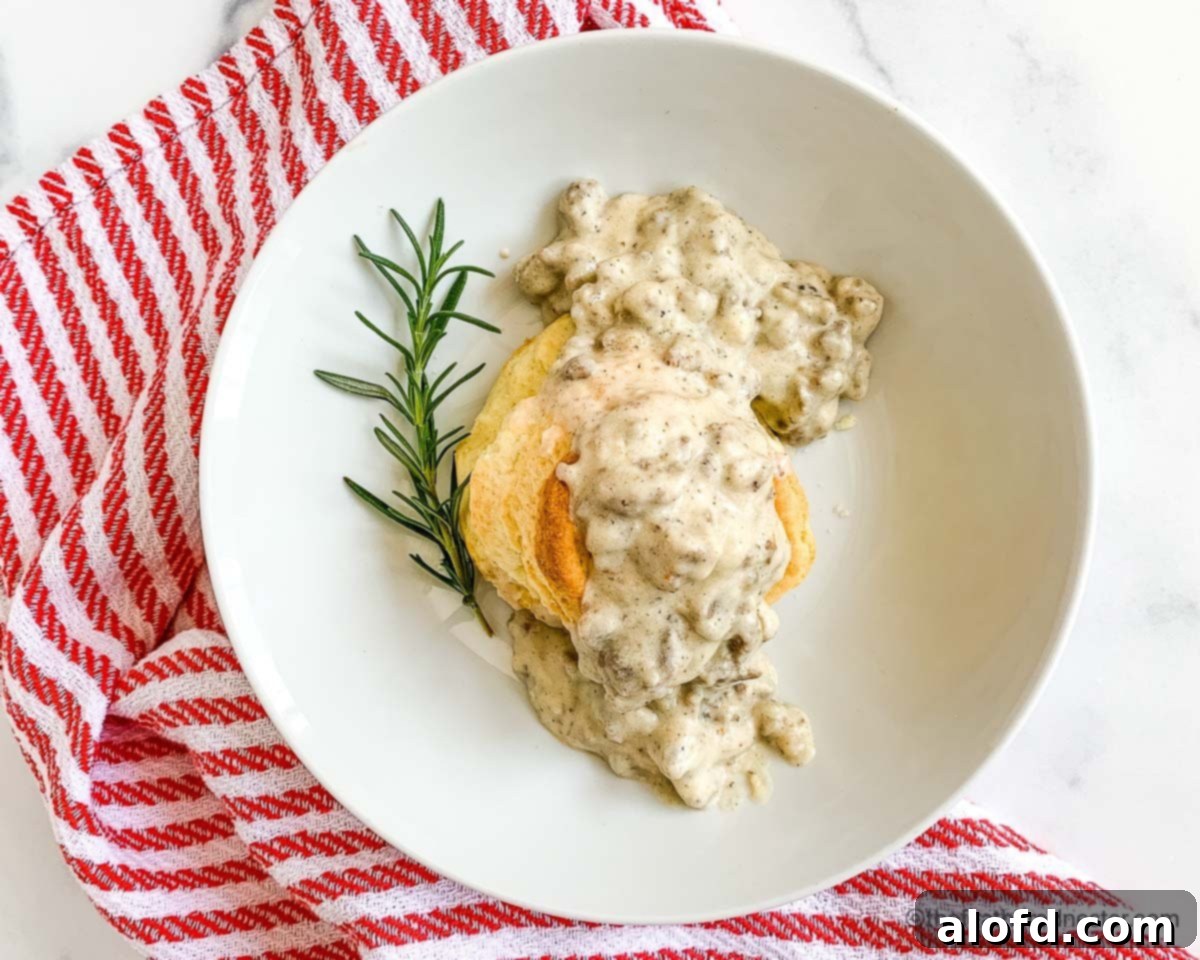 A white plate filled with fluffy biscuits generously topped with creamy turkey gravy, garnished with fresh parsley and served with a red and white checkered napkin, ready for a comforting meal.