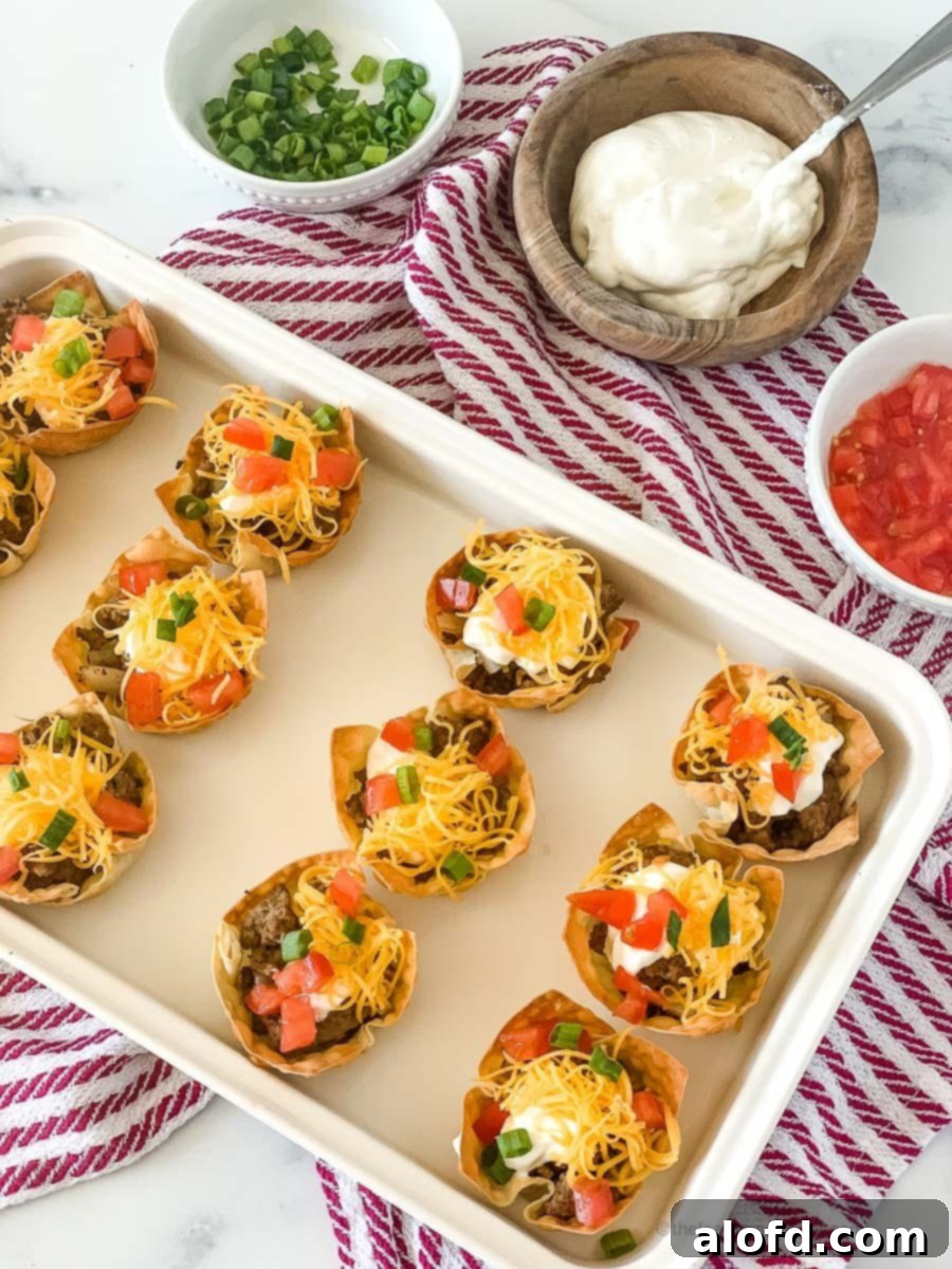 Crispy Taco Wonton Bites 2 A white tray of crispy taco wonton cups elegantly arranged on a festive red and white napkin, surrounded by small bowls of fresh cilantro, creamy sour cream, and zesty salsa. The perfect spread for any gathering.