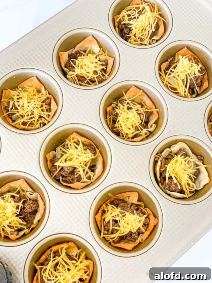 Crispy Taco Wonton Bites 8 A muffin tin showcasing wonton cups filled with seasoned ground beef and topped with a generous layer of shredded cheese, ready for final baking.