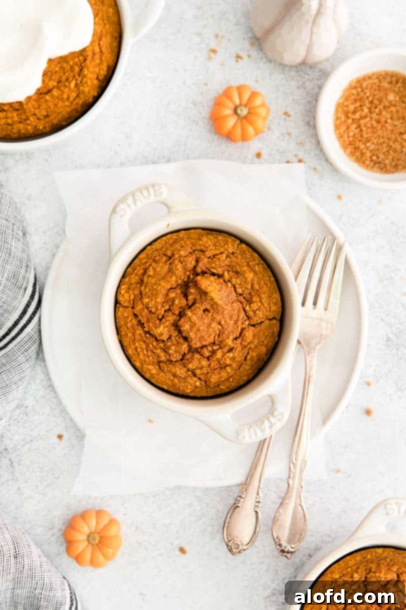 A beautifully set fall breakfast table features white plates, gleaming silverware, and soft cloth napkins, all accentuating a delicious ramekin of healthy pumpkin baked oats, inviting a cozy morning meal.