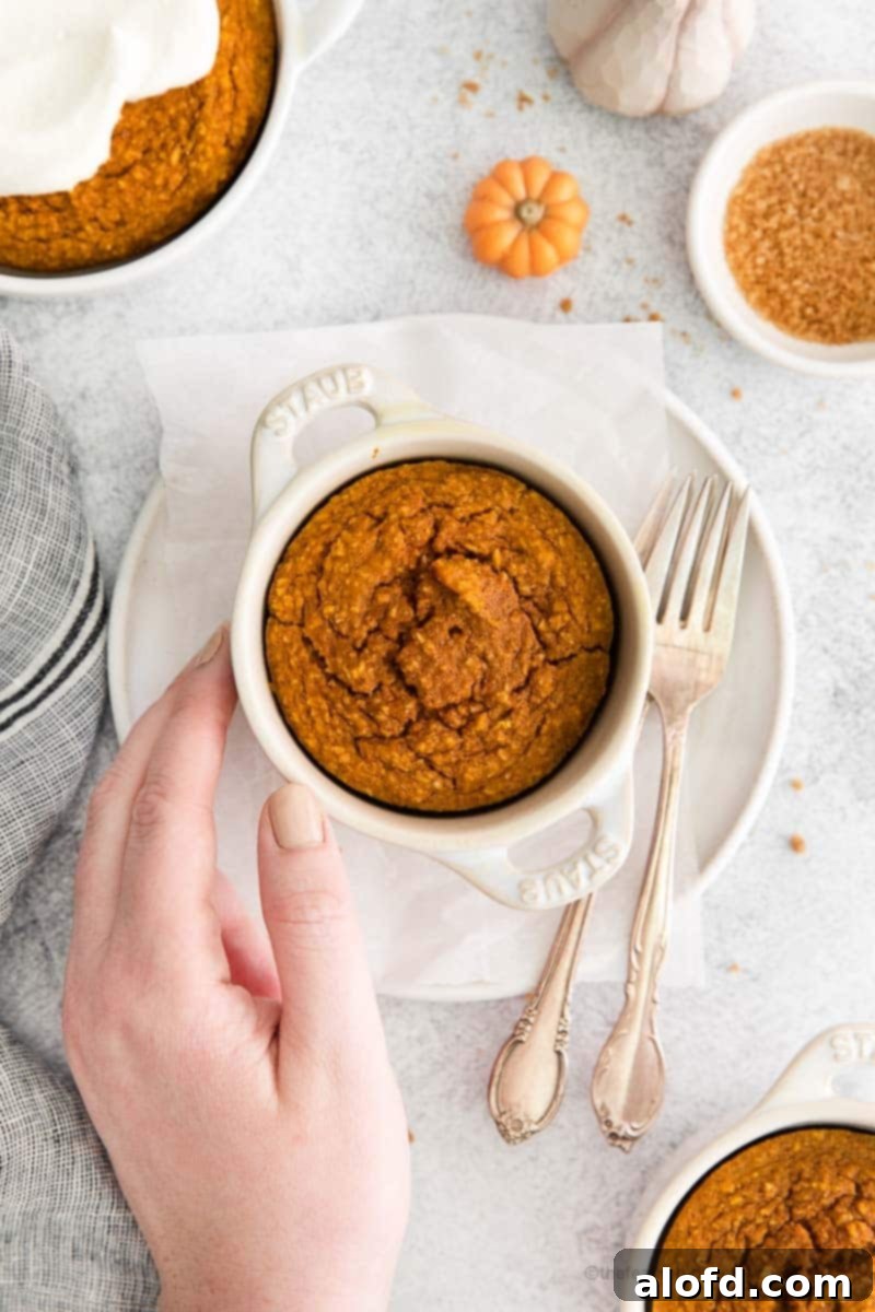 A close-up shot of pumpkin spiced oatmeal, beautifully baked into a round Staub cocotte, served elegantly on a white plate with a single fork resting beside it, highlighting its rich, comforting texture.