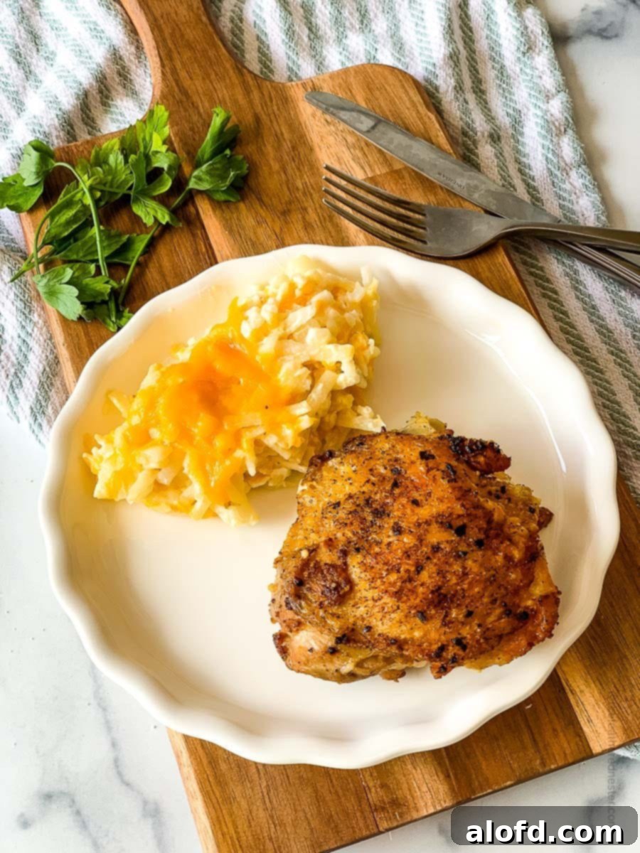 Golden-Crisp Cast Iron Chicken Thighs 2 A white plate with perfectly cooked cast iron chicken thighs and cheesy hash browns, showcasing crispy skin and tender meat.