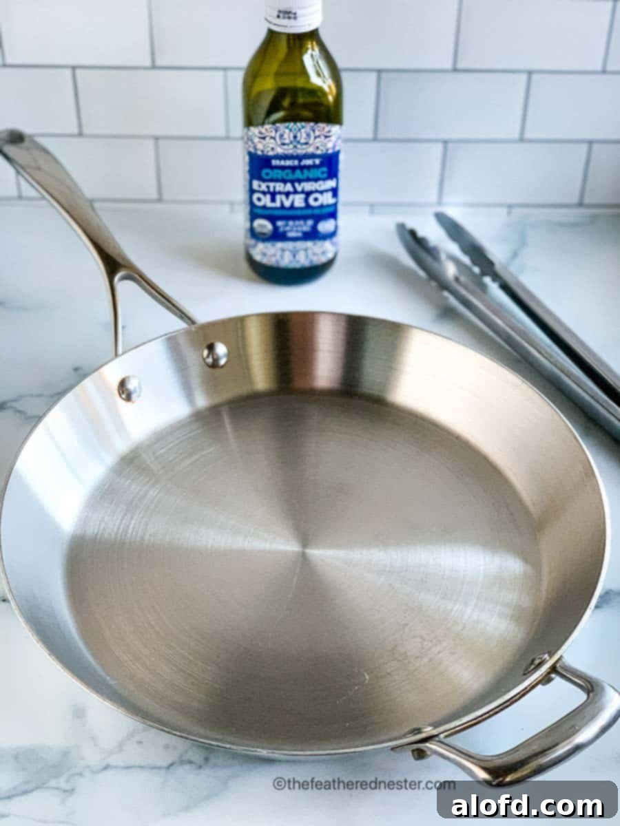 Golden-Crisp Cast Iron Chicken Thighs 4 A pristine stainless steel skillet, ready for cooking, sits on a clean countertop.