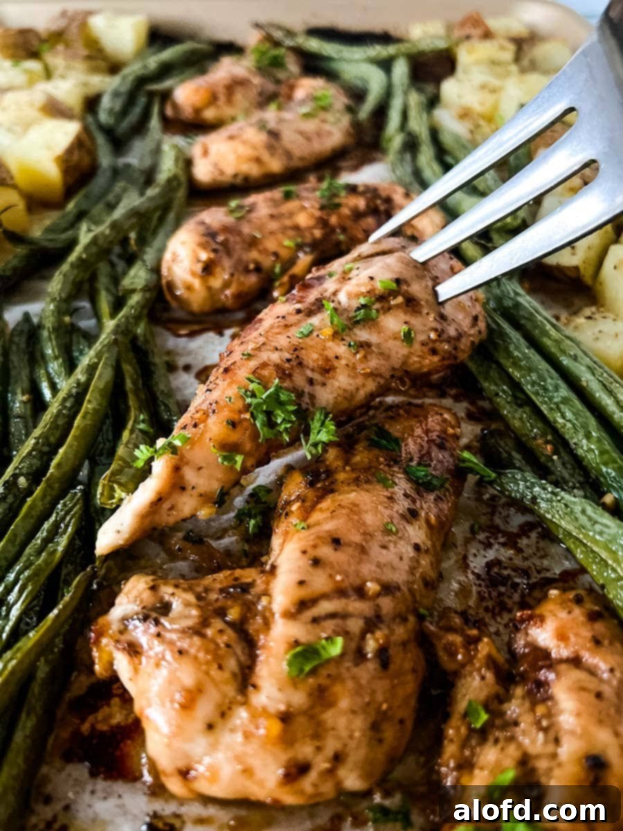 Flavorful oven baked marinated chicken tenders served with a fork, alongside perfectly roasted asparagus and potatoes.