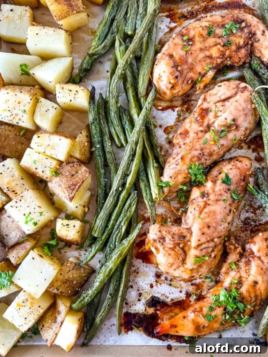Succulent baked chicken tenders nestled beside golden roasted potatoes and vibrant green asparagus, making for a wholesome and appealing meal.