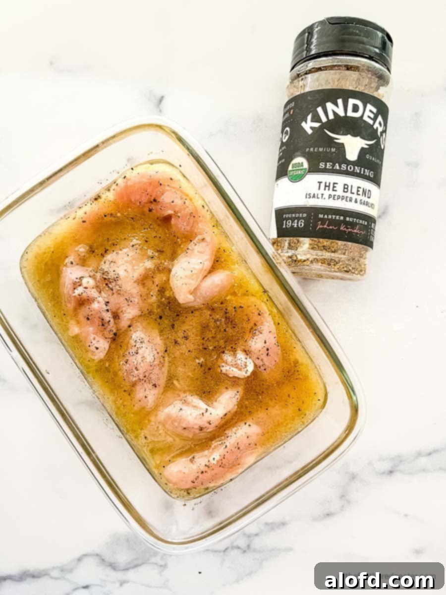 A glass container filled with chicken tenders soaking in a flavorful marinade, with a bottle of Italian seasoning positioned nearby, highlighting the key ingredients for marination.