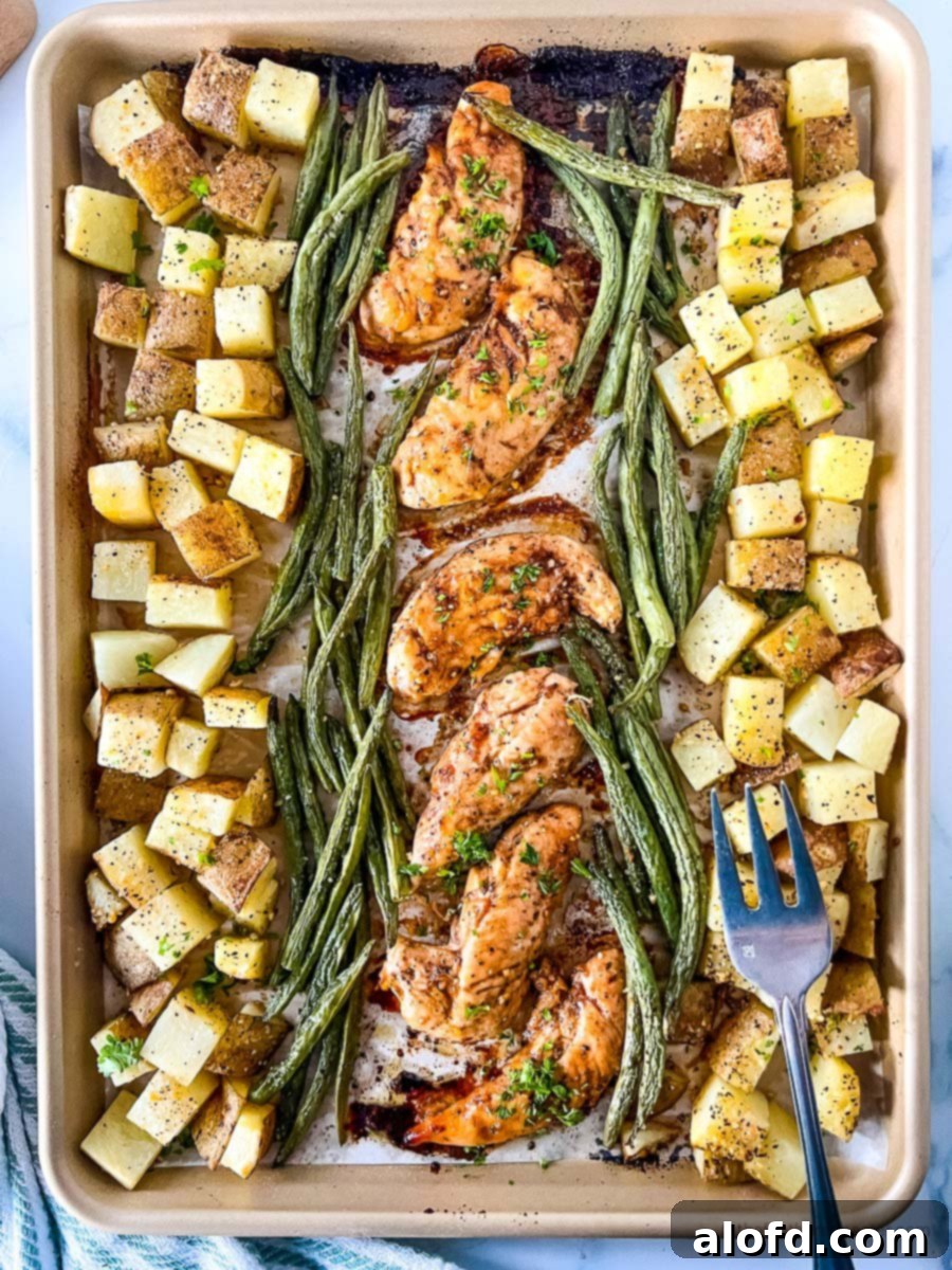 A freshly baked sheet pan meal featuring golden-brown oven baked marinated chicken tenders, alongside tender asparagus and roasted potatoes, with a fork poised for serving.