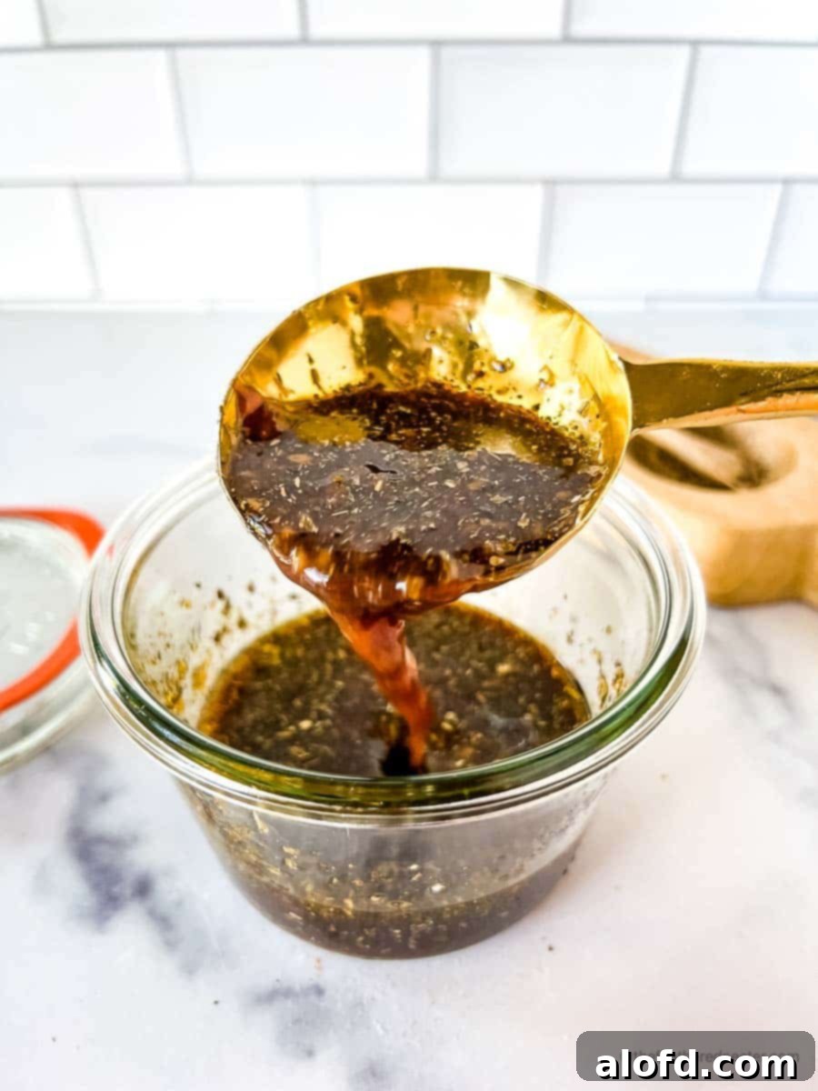 Sweet and Tangy Balsamic Chicken Marinade 2 A golden spoon scooping the balsamic marinade for chicken in a glass jar with its lid and a salt cellar in the background.