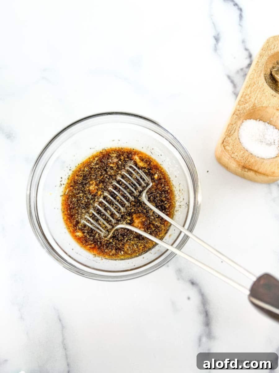 Sweet and Tangy Balsamic Chicken Marinade 6 Whisking the balsamic vinegar marinade for chicken ingredients in a clear bowl with a salt and pepper cellar in the background.