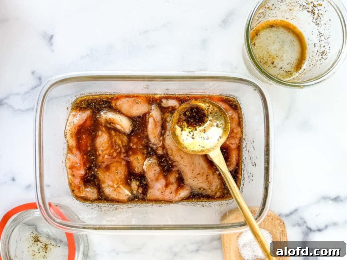 Sweet and Tangy Balsamic Chicken Marinade 8 Marinated chicken placed in a glass container with a golden spoon on it and small bowls and salt cellar in the background.