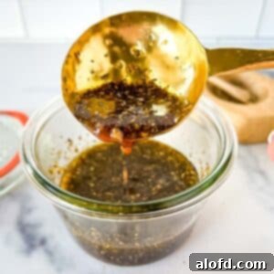Sweet and Tangy Balsamic Chicken Marinade 9 A close up photo of a golden spoon scooping the Balsamic chicken marinade in a glass jar with its lid and a salt cellar in the background.