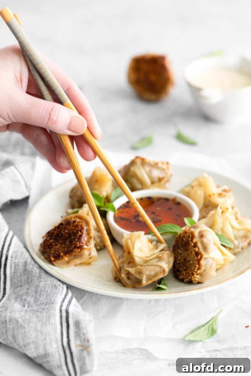 Umami Mushroom Pockets 13 A hand holds a chopstick, elegantly picking up a single vegetarian dumpling from a plate, highlighting its perfect form and texture, ready for enjoyment.