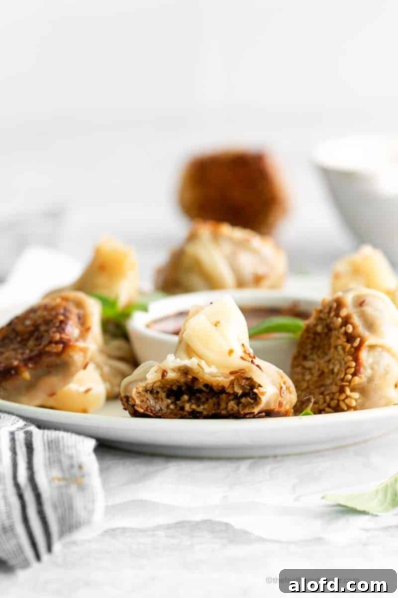 Umami Mushroom Pockets 3 A close-up, side view of perfectly cooked mushroom dumplings elegantly presented on a plate, with a small dish of shimmering garlic chili oil positioned invitingly at the center.