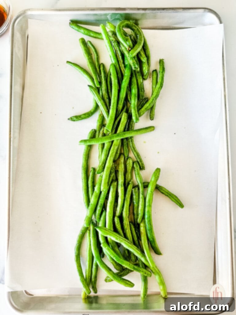Effortless Sheet Pan Pork Tenderloin 5 Uncooked string beans on a baking pan lined with parchment paper.