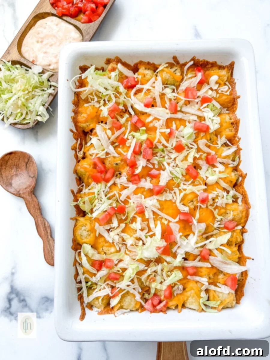 A hearty Cheeseburger Tater Tot Casserole in a white baking dish, ready to be served, garnished with fresh lettuce and tomato.