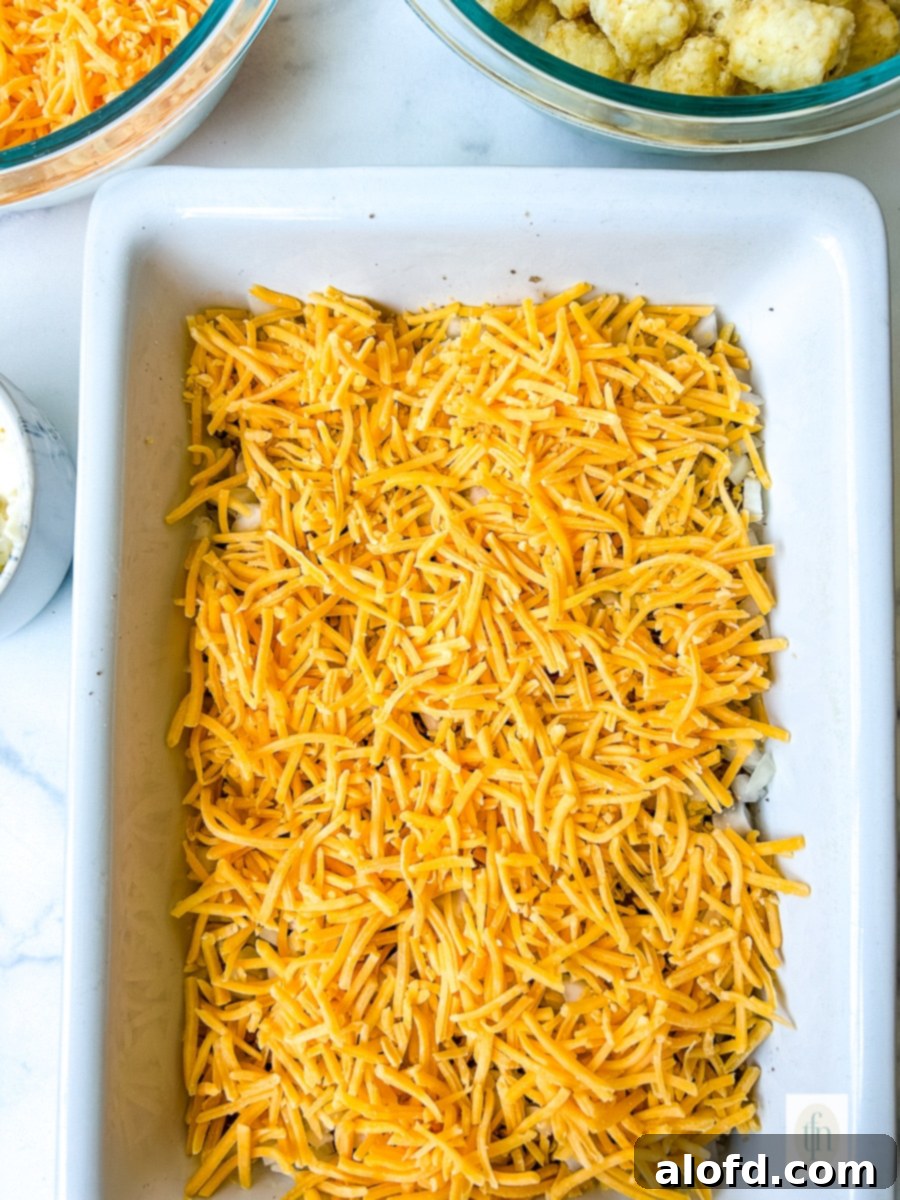 Shredded cheddar cheese layered into a baking dish over the ground beef and American cheese base, a key step for Cheeseburger Tater Tot Casserole.