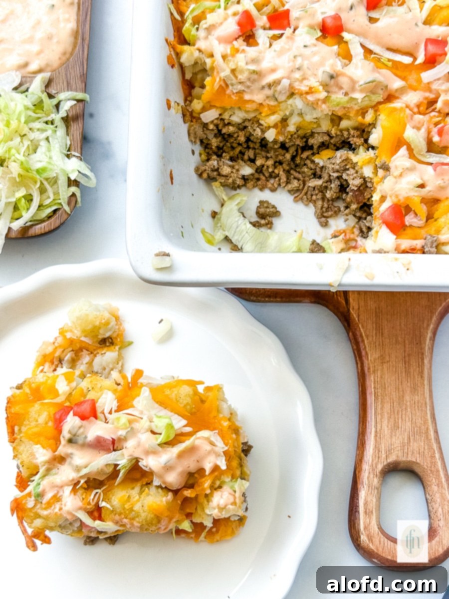 A plated serving of Cheeseburger Tater Tot Casserole next to the remaining casserole in a white baking dish, garnished with fresh lettuce and sauce.