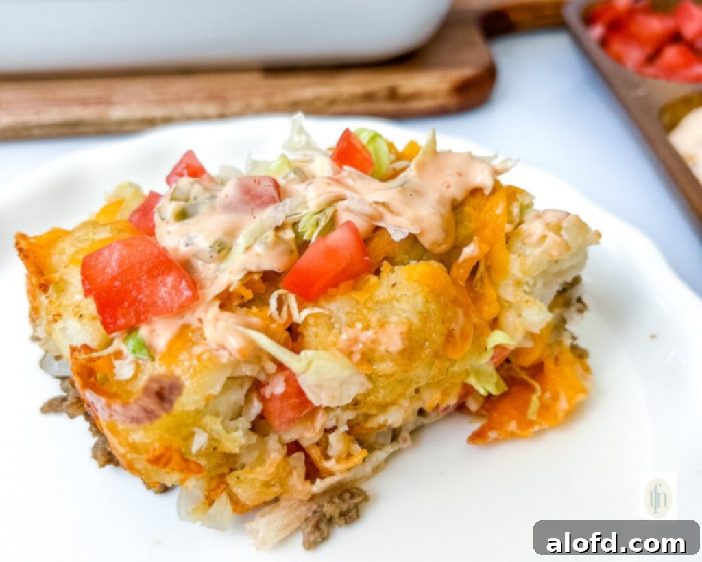 Close up of a baked comfort food meal: Cheeseburger Tater Tot Casserole with ground beef, crispy potatoes, melted cheese, fresh tomatoes, and shredded lettuce, ready for enjoyment.
