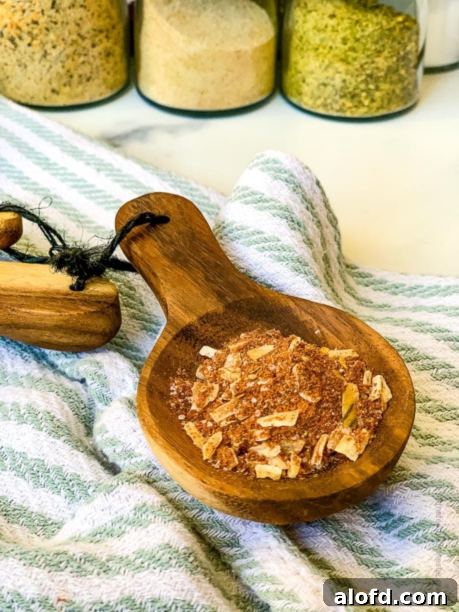 Ultimate Chicken Taco Mix 2 A wooden measuring spoon with chicken taco seasoning with striped kitchen cloth and seasonings in the background.