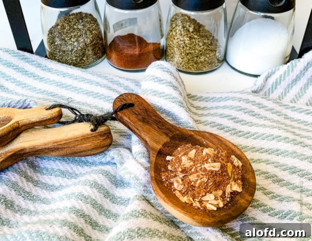 Ultimate Chicken Taco Mix 9 A wide horizontal photo of a wooden measuring spoon with chicken taco spice mix with striped kitchen cloth and seasonings in the background.