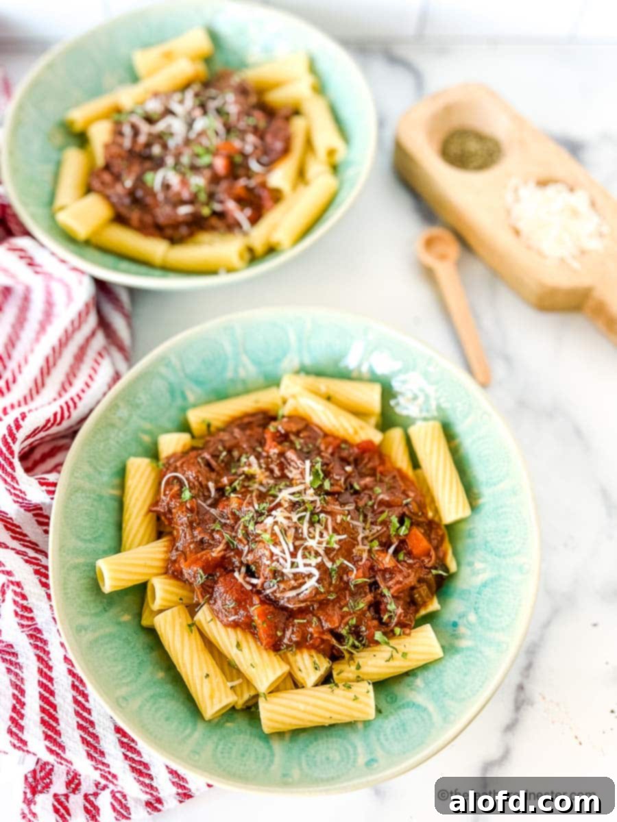 Braised Short Rib Rigatoni 12 Two vibrant green bowls filled with short rib rigatoni, tastefully arranged with a striped red cloth and salt and pepper shakers in the background.