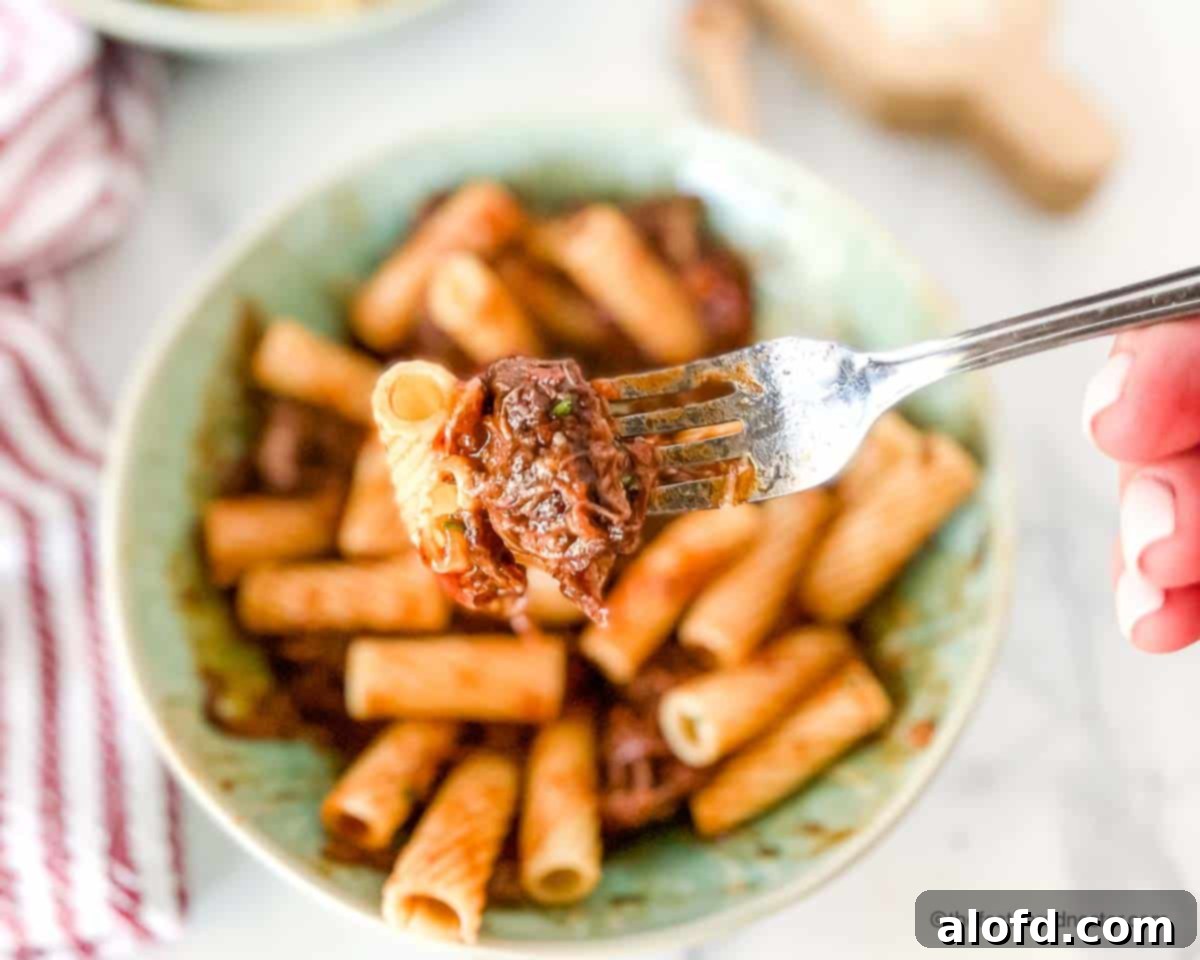 Braised Short Rib Rigatoni 14 A fork holding a piece of pasta and a generous portion of short rib ragu, with a full bowl of short rib rigatoni blurred in the background, showcasing the deliciousness.