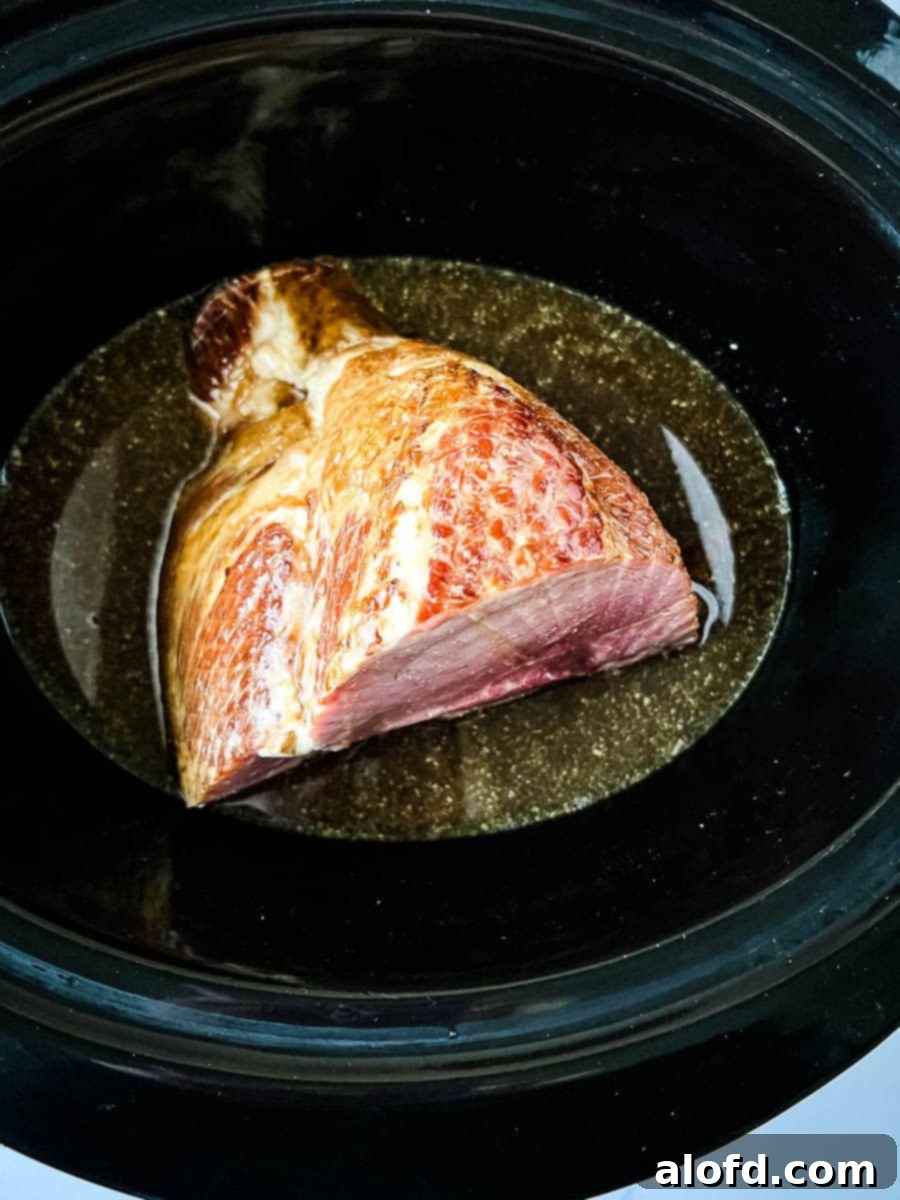 A spiral-sliced Dr. Pepper ham sits snugly in a slow cooker, already coated with the sweet and savory glaze, ready for cooking. The pot is almost full, promising a tender, flavorful meal.