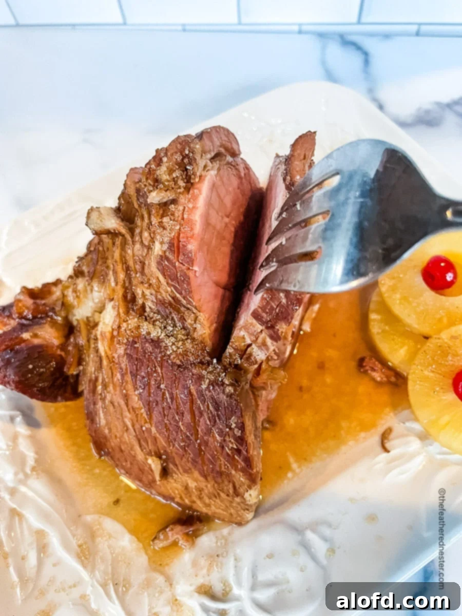 A beautifully glazed and cooked Dr. Pepper ham, glistening with a rich, dark glaze, is presented on a clean white plate. Pineapple slices adorn the side, and a carving fork is poised, ready to serve this sweet and tangy holiday entree.