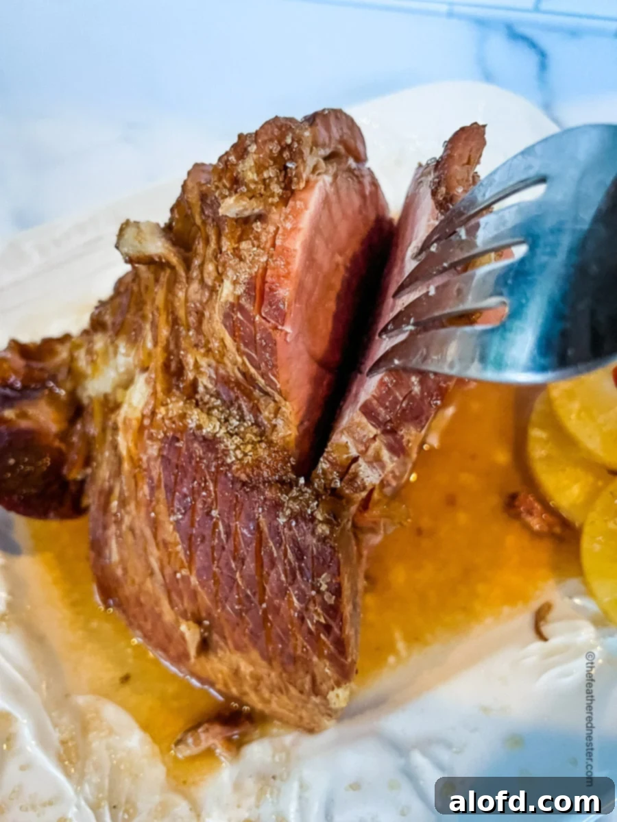 A close-up view of a carving fork gently holding a piece of tender, spiral-sliced Dr. Pepper ham, showcasing its juicy texture and the rich, glistening glaze. The background is softly blurred, keeping the focus on the mouth-watering detail of the meat.