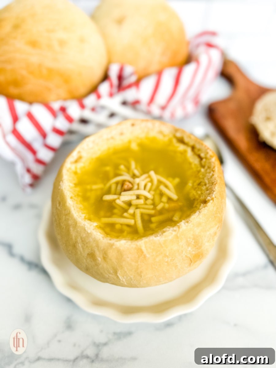 Artisan Sourdough Soup Bowls 12 A generously filled sourdough bread bowl with a creamy, vibrant soup, presented on a simple white plate against a light background. A spoon rests in the bowl, ready for enjoyment.