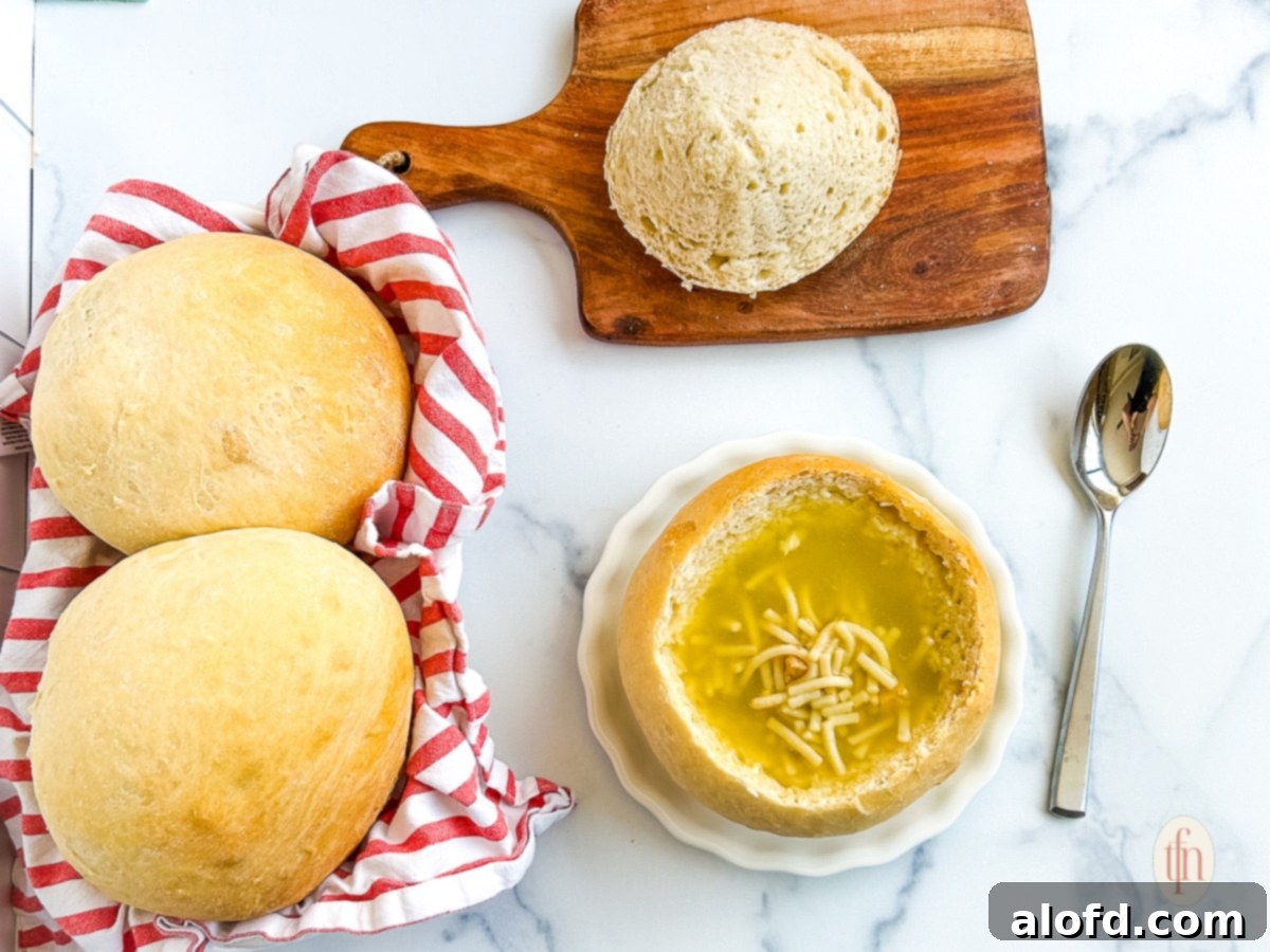 Artisan Sourdough Soup Bowls 13 Two golden-crusted sourdough bread bowls, one filled with creamy soup and the other untouched, resting on a white plate on a white background. The untouched bowl highlights the rustic texture and deep golden hue of the crust.