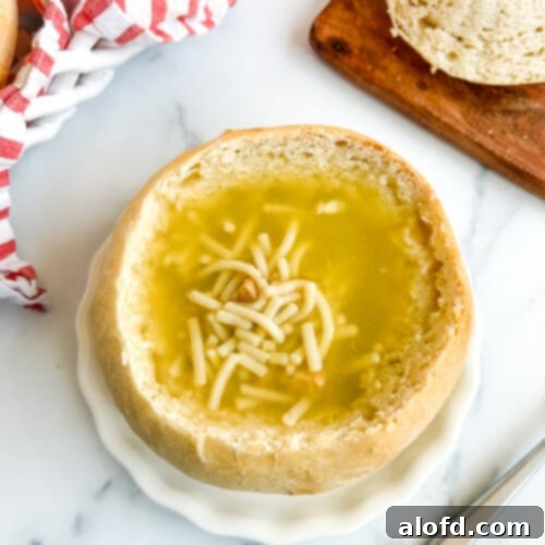 Artisan Sourdough Soup Bowls 14 A sourdough bread bowl filled with a creamy, rich soup, served on a white plate against a clean white background. The steam gently rises from the soup, enhancing its inviting appeal.