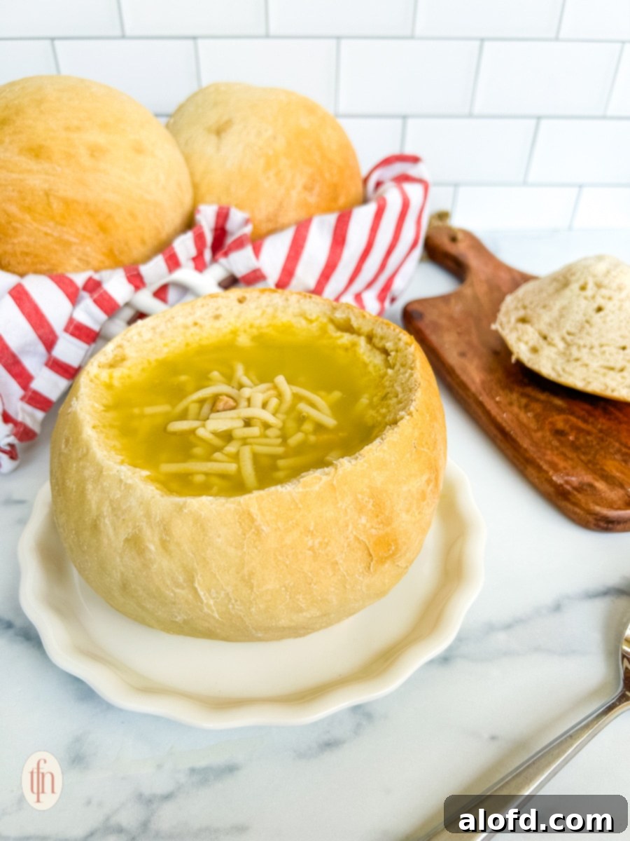 Artisan Sourdough Soup Bowls 3 A close-up view of a sourdough bread bowl, artfully carved out and brimming with a creamy, vibrant orange soup. The bowl is presented on a pristine white plate, with the rustic texture of the bread clearly visible.