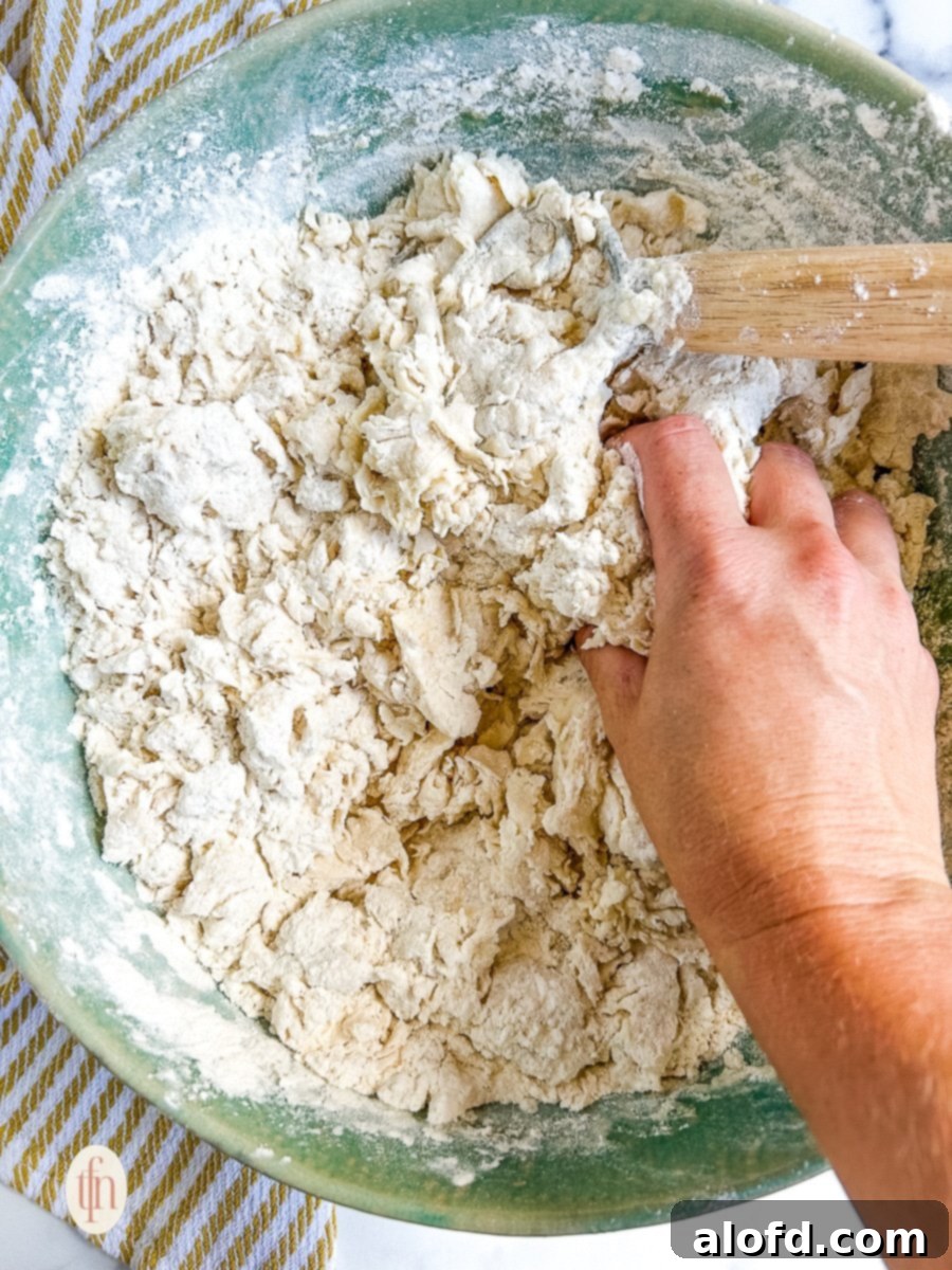 Artisan Sourdough Soup Bowls 7 A close-up of hands mixing a sticky sourdough bread dough in a large bowl, demonstrating the manual kneading process to incorporate ingredients thoroughly.