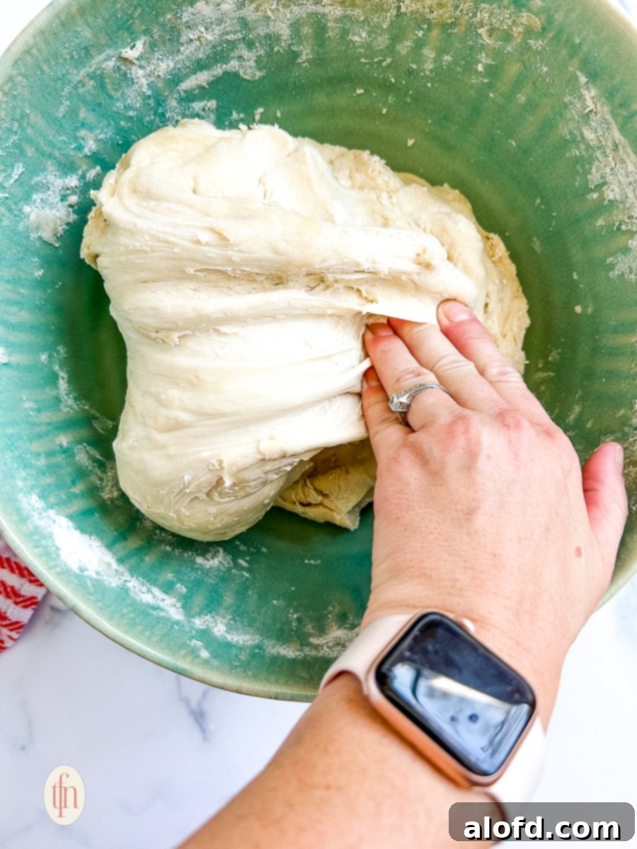 Artisan Sourdough Soup Bowls 8 A hand gently pulling and folding a portion of soft, sticky sourdough dough on a lightly floured surface, demonstrating the stretch-and-fold technique for gluten development.