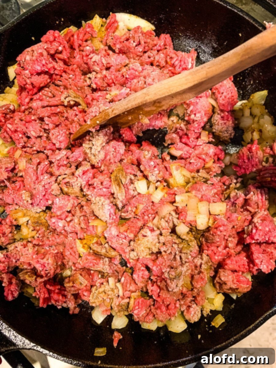 Loaded Taco Bake 6 Close-up of seasoned ground beef cooking in a skillet, being broken up with a spatula.