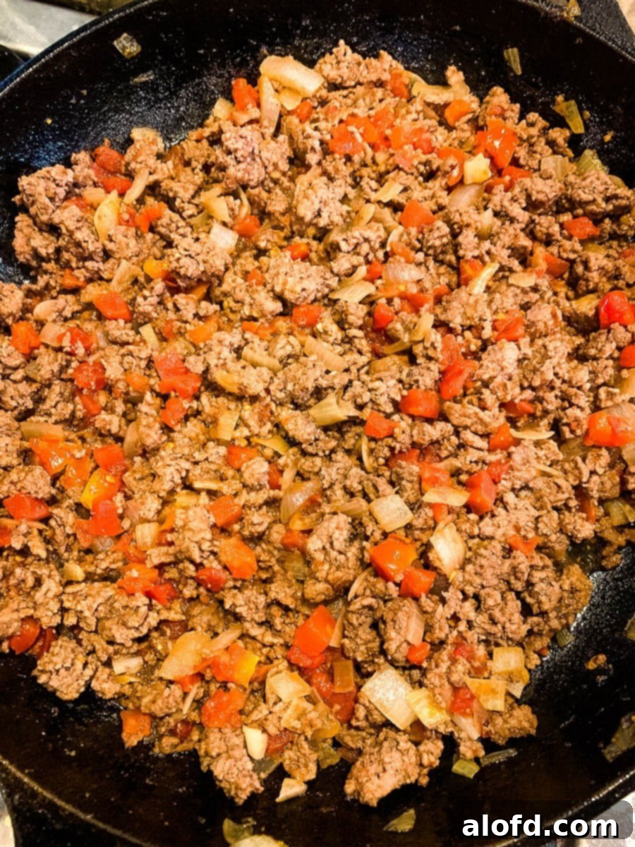 Loaded Taco Bake 7 The savory mixture of browned meat, diced tomatoes, and onions simmering in a pan, reducing liquid.