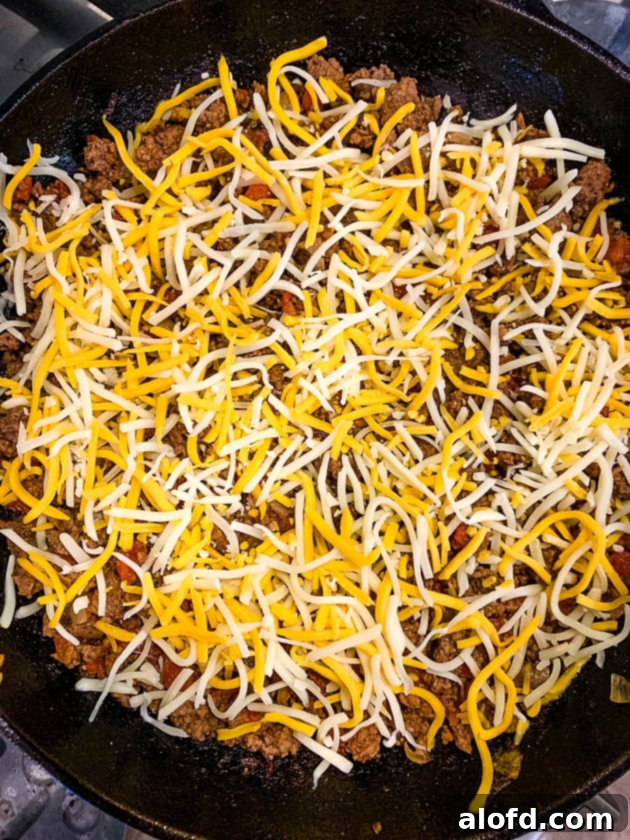 Loaded Taco Bake 8 A delicious layer of shredded Mexican cheese blend distributed over the cooked taco meat in a skillet, ready for Fritos.