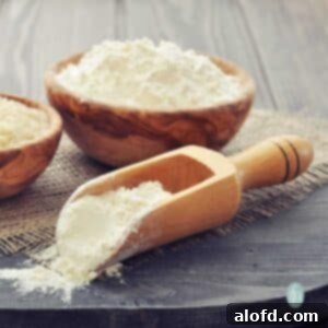 Self rising flour in a wooden scoop and a wooden bowl, sitting on a piece of burlap.